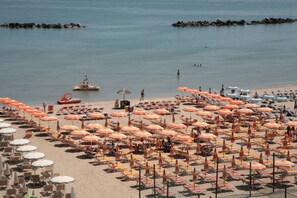A beach with rows of sun loungers and umbrellas, a boat, and rocky outcrops in the water. - Residence San Paolo (Ravenna)
