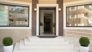 A modern building entrance with a set of steps leading to a door, flanked by two potted plants. - Residence San Paolo (Ravenna)