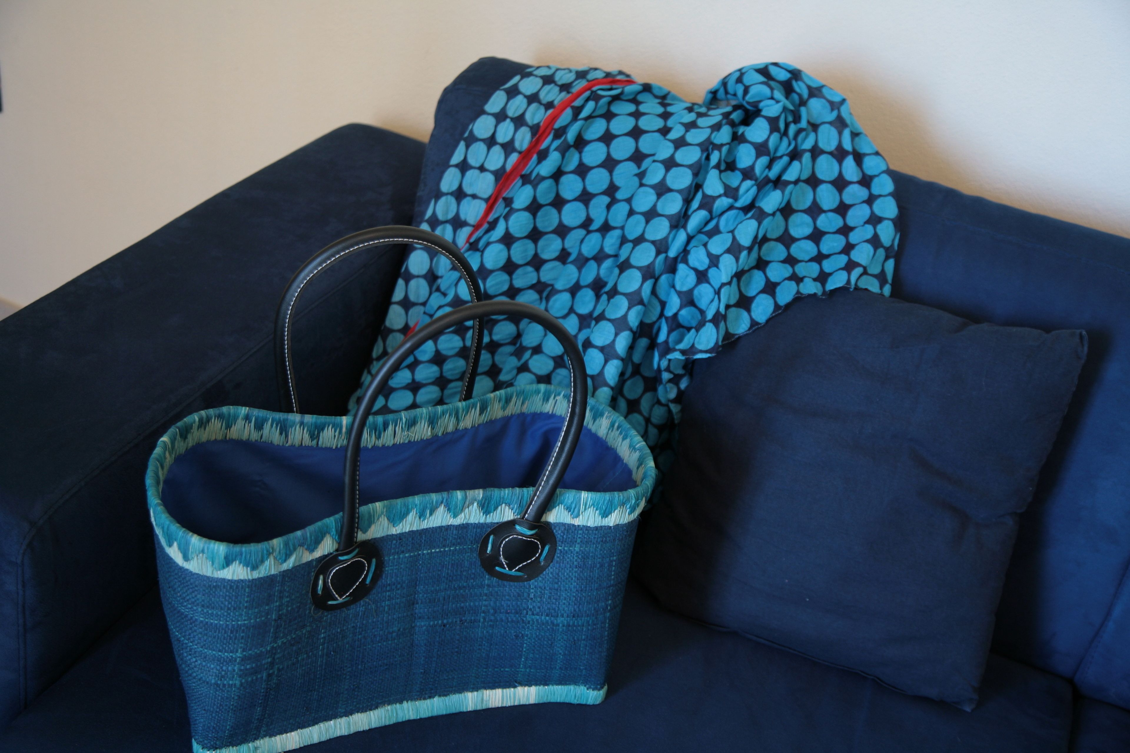 Ein dunkelblaues Sofa mit einer blau gepunkteten Decke und einer Jeanshandtasche mit schwarzen Tragegriffen.