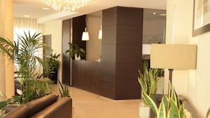 A modern reception area with a curved reception desk, a seating area with a sofa, and a potted plant arrangement. - Residence San Paolo (Ravenna)