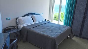 Una habitación de hotel con cama, escritorio, silla, ventana con cortinas y vista al mar.