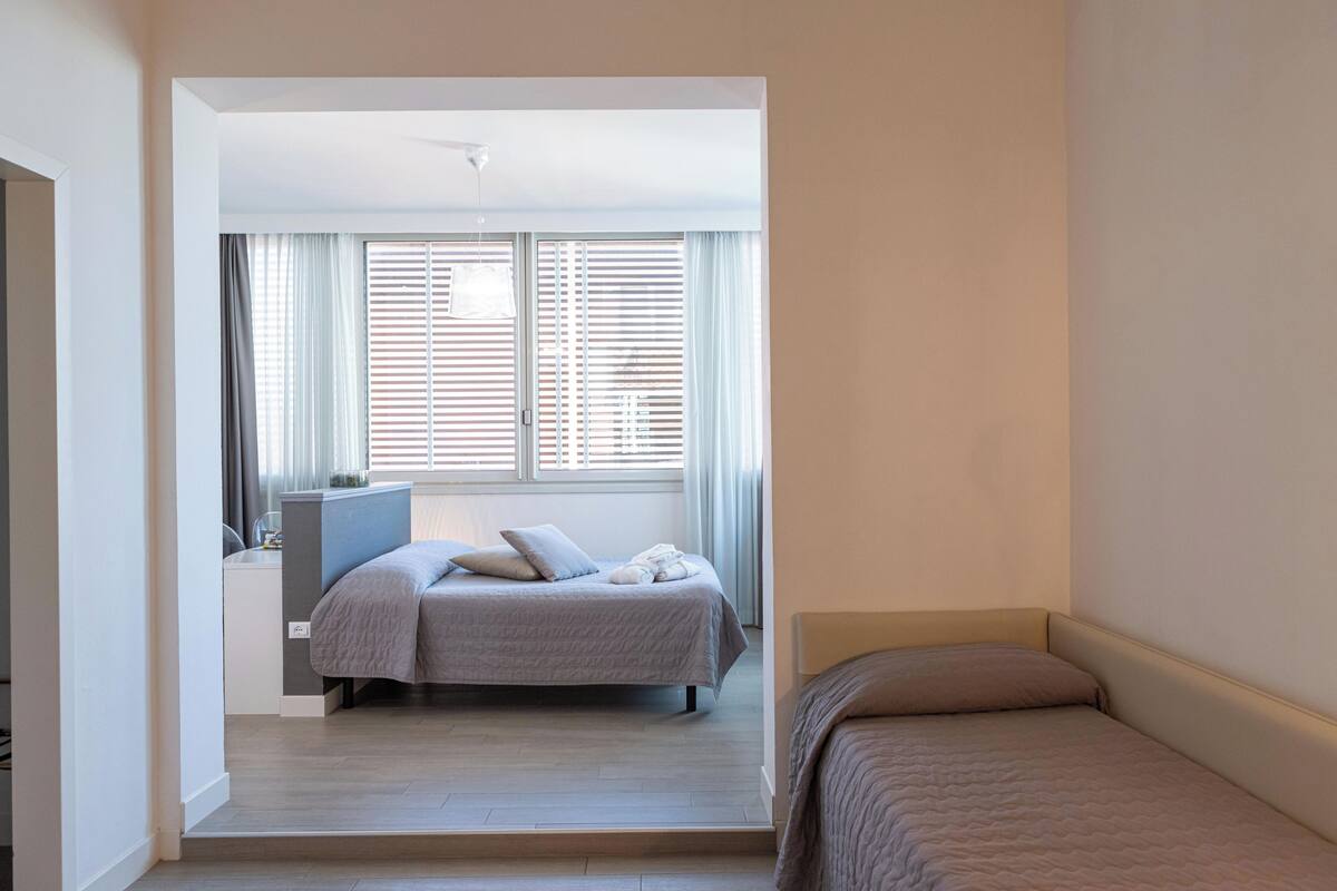 A bedroom with two beds, a desk, and a window with blinds.
