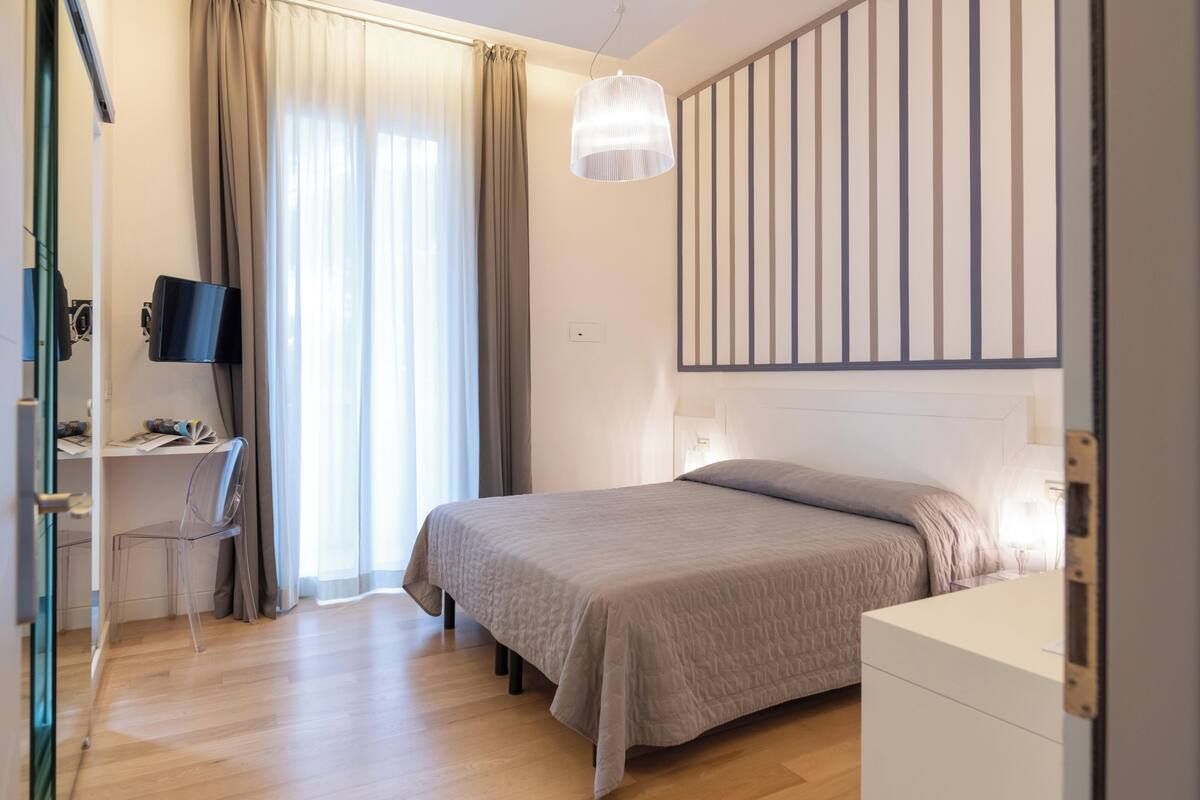 A modern bedroom with a bed, desk, chair, and a TV.