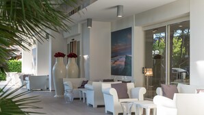 A modern lounge area with white sofas, a large vase with red flowers, and a painting of a landscape. - Perla Verde Hotel (Cervia)