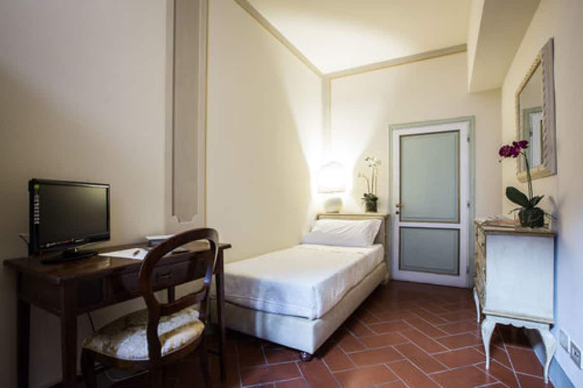 A small, compact room with a bed, a desk with a computer, a chair, and a small table with a plant.
