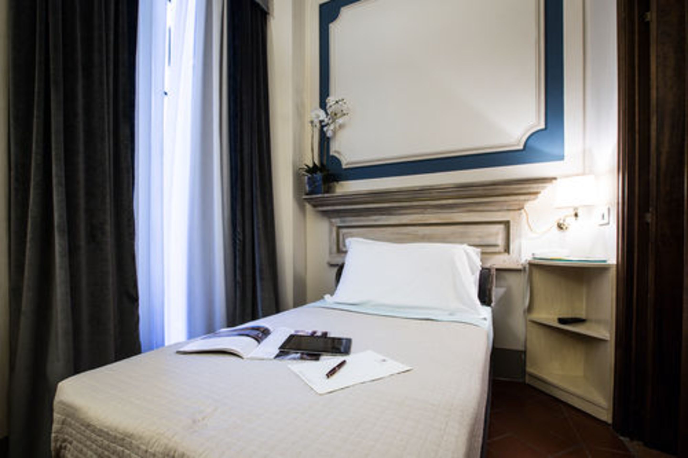 A hotel room with a bed, a nightstand, a lamp, and a window with curtains.