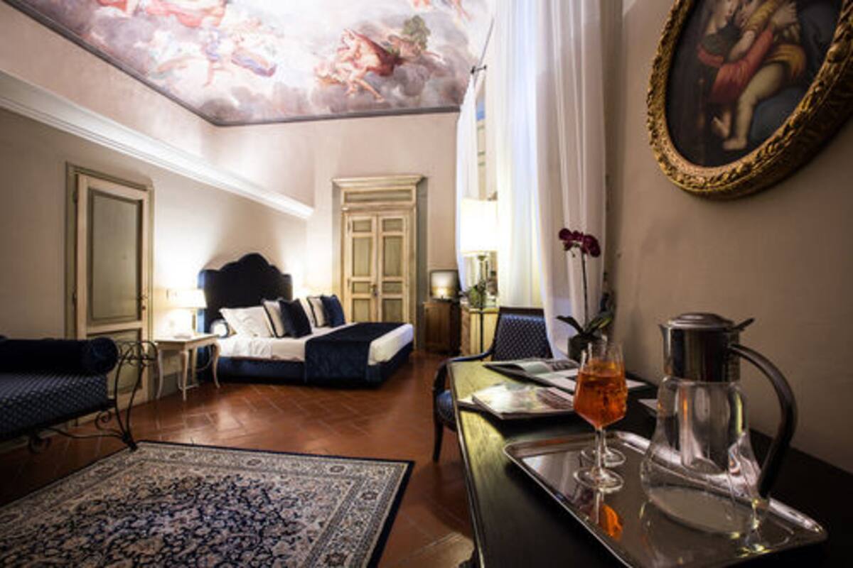 A hotel room with a bed, a sitting area with a table and chairs, a coffee pot, and a framed painting on the wall.