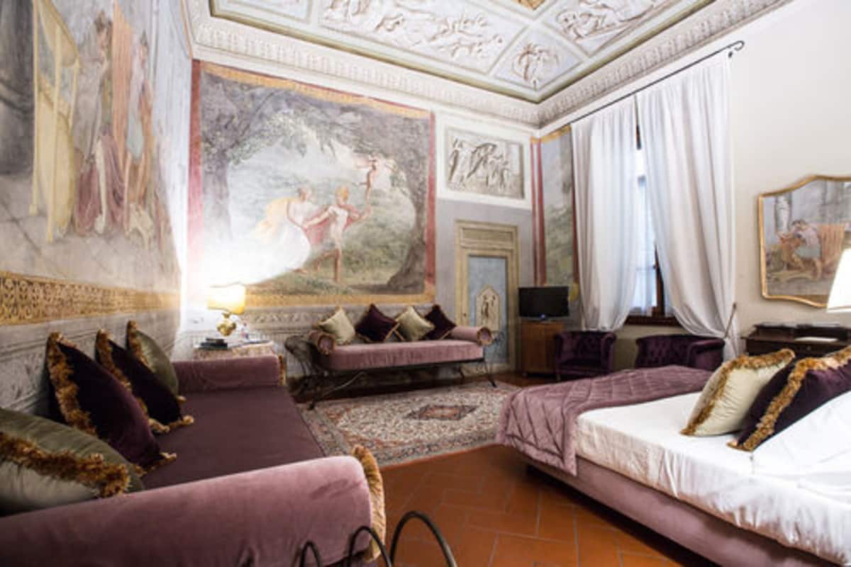A room with a large mural, a bed, a sofa, and a television.