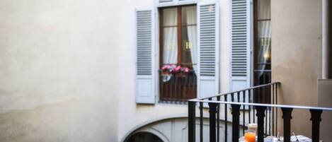 A balcony with a table, a chair, and a window with shutters.