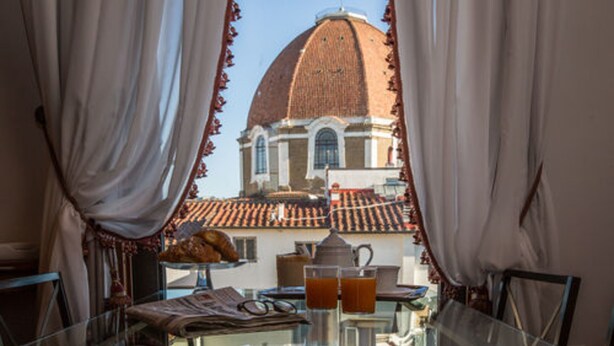 A dining table with a view of a building with a dome and tiled roof through sheer curtains. - Hotel Burchianti (Florence)