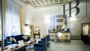 A spacious living room with a blue sofa, a coffee table, and a glass coffee table. There is a large mirror on the wall and a chandelier. - Hotel Burchianti (Florence)