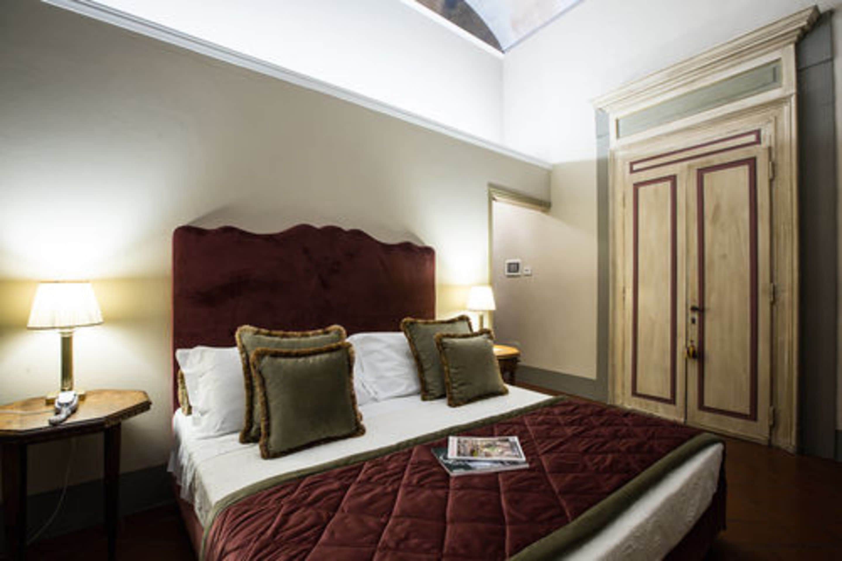 A hotel room with a large bed, two bedside tables with lamps, a wardrobe, and a skylight.