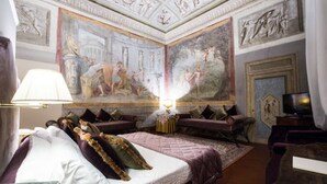 A luxurious hotel room with a large bed, a desk, a television, and a mural on the ceiling. - Hotel Burchianti (Florence)