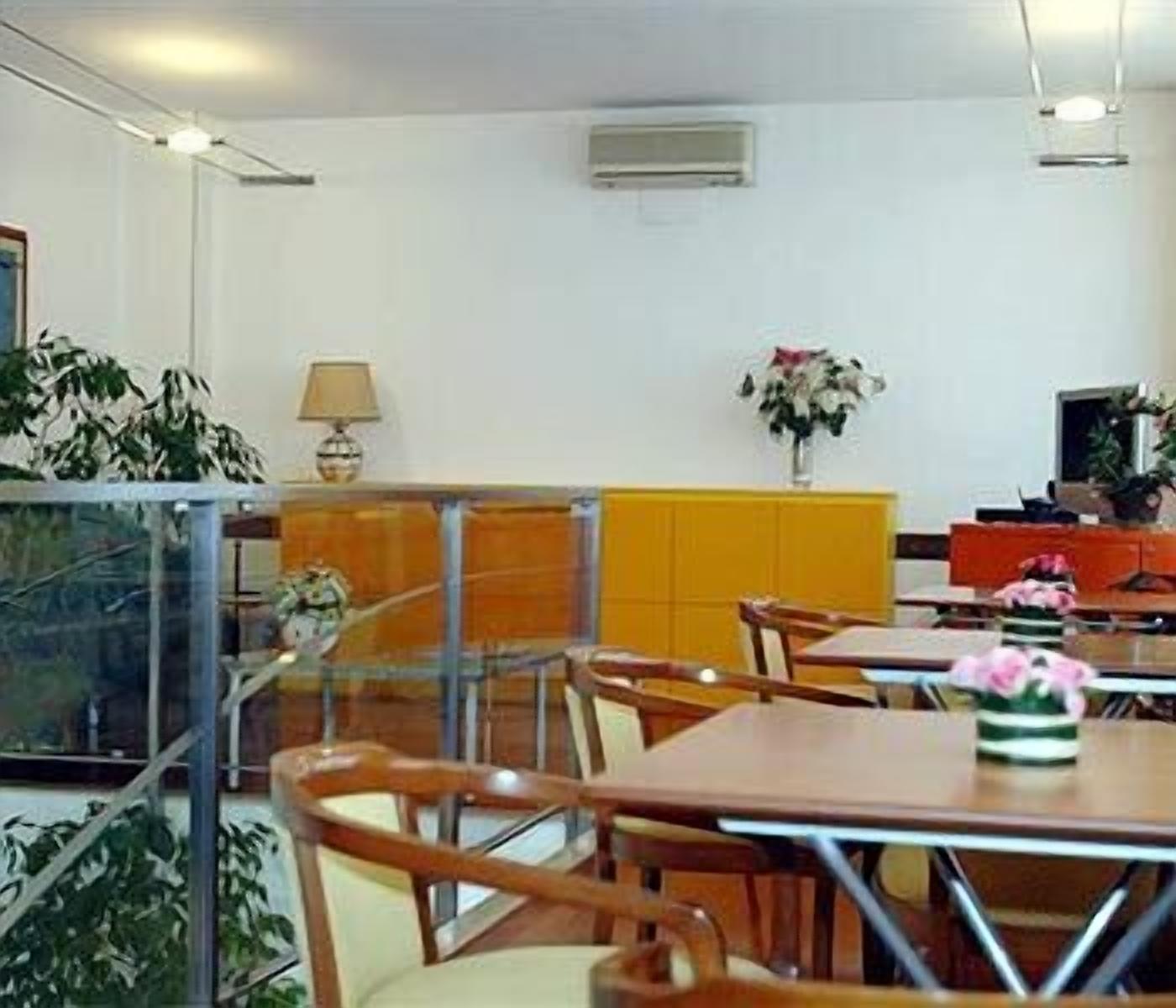 A dining area with wooden tables and chairs, a yellow cabinet, and a potted plant.