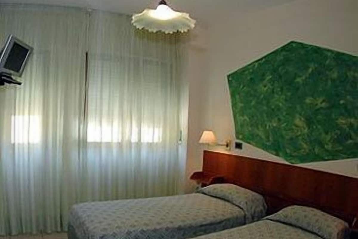 Hotellihuone, jossa on kaksi sänkyä, seinälle asennettu televisio, lamppu ja vihreäkuvioinen seinä.