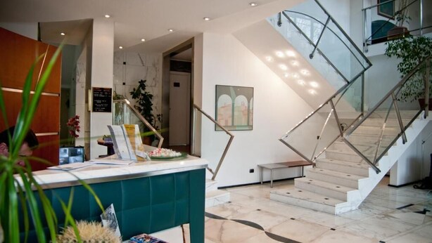 Un moderno vestíbulo de hotel con mostrador de recepción, una escalera con barandillas de vidrio y un mural en la pared.