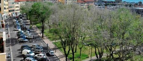 A street lined with parked cars and buildings, a clear sky, and a body of water in the distance.