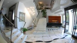 Un vestíbulo amplio con piso de mármol, una escalera y una zona de estar con sofá y mesa de centro.