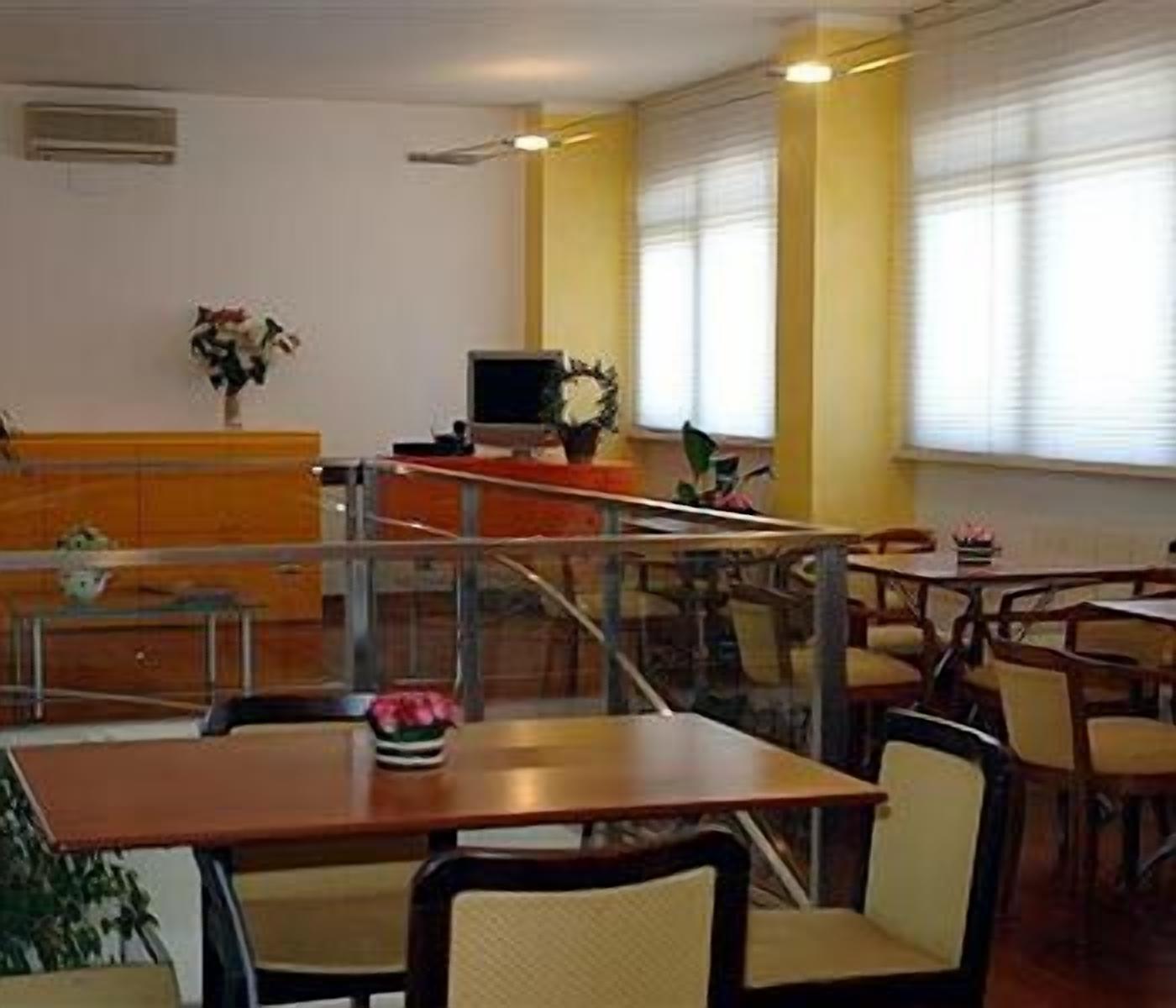 A dining area with tables and chairs, a counter with a computer, and a window with blinds.