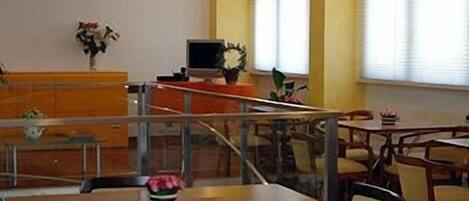 A dining area with tables and chairs, a counter with a computer, and a window with blinds.