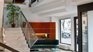 Un interior moderno con una escalera de mármol, un sofá verde y un amplio ventanal con vista a coches estacionados.