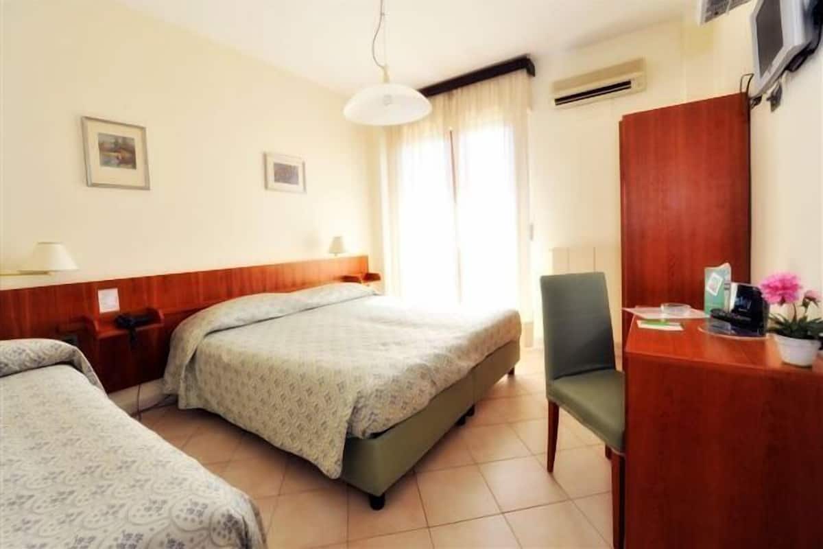 Hotellihuone, jossa on kaksi sänkyä, työpöytä, tuoli ja vaatekaappi.