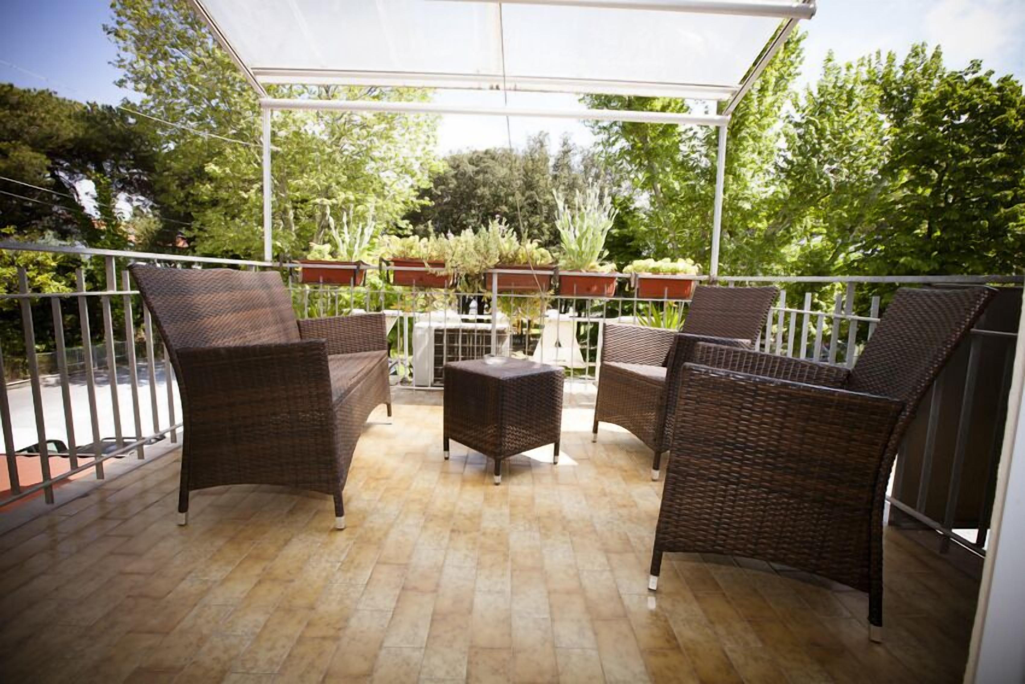 Een overdekt terras met rieten meubels en potplanten.