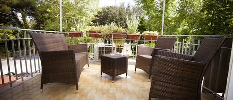 Een overdekt terras met rieten meubels en potplanten.