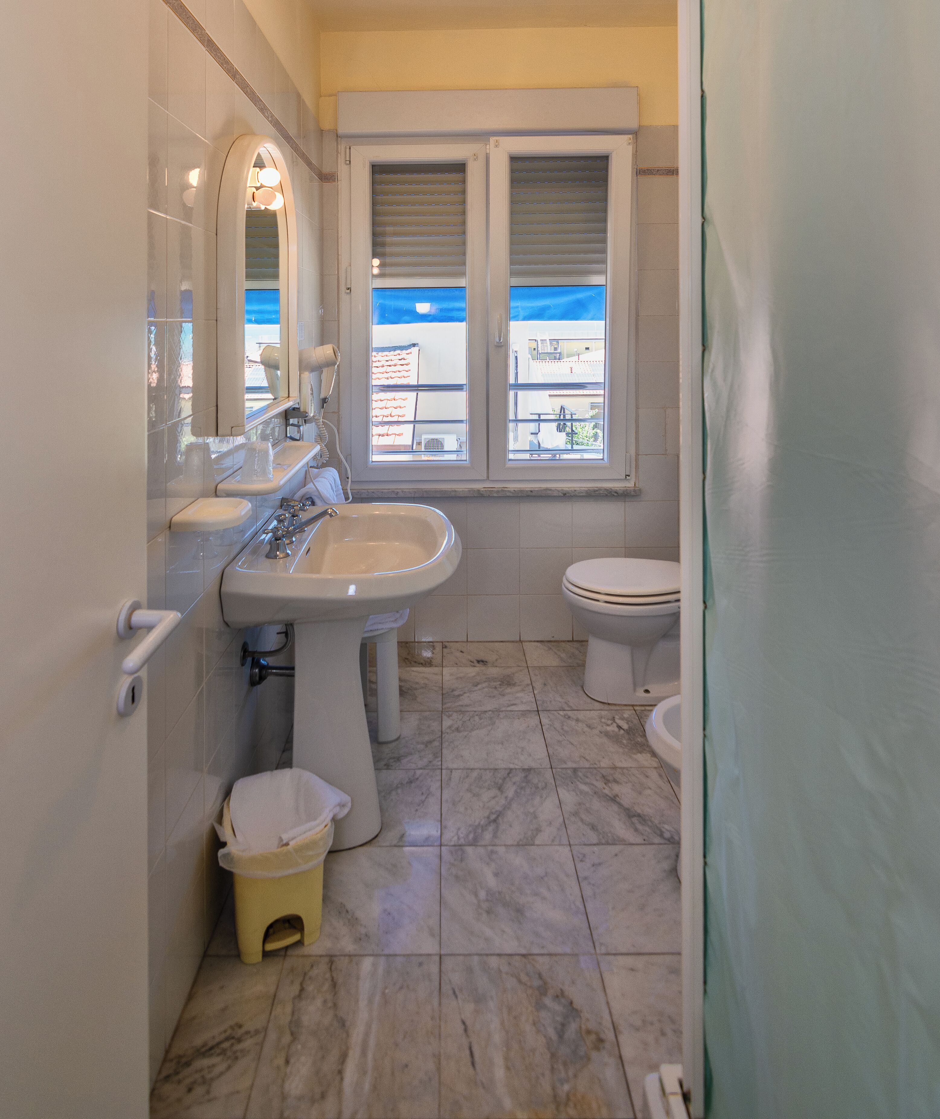 Ein Badezimmer mit Waschbecken, Toilette und einem Fenster mit Blick auf Gebäude.