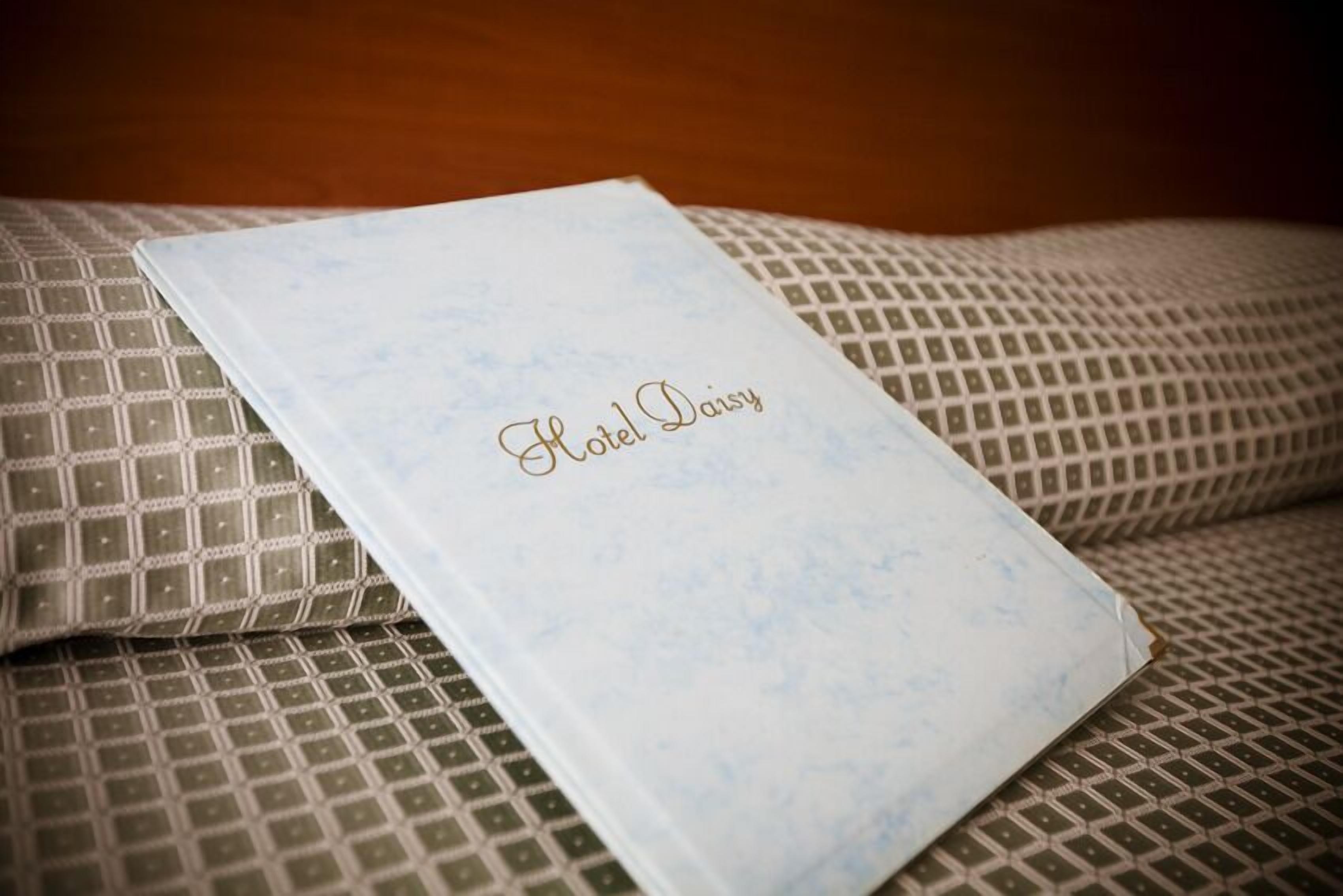 A hotel room with a patterned bedspread and a white booklet with "Hotel Daisy" written on it.