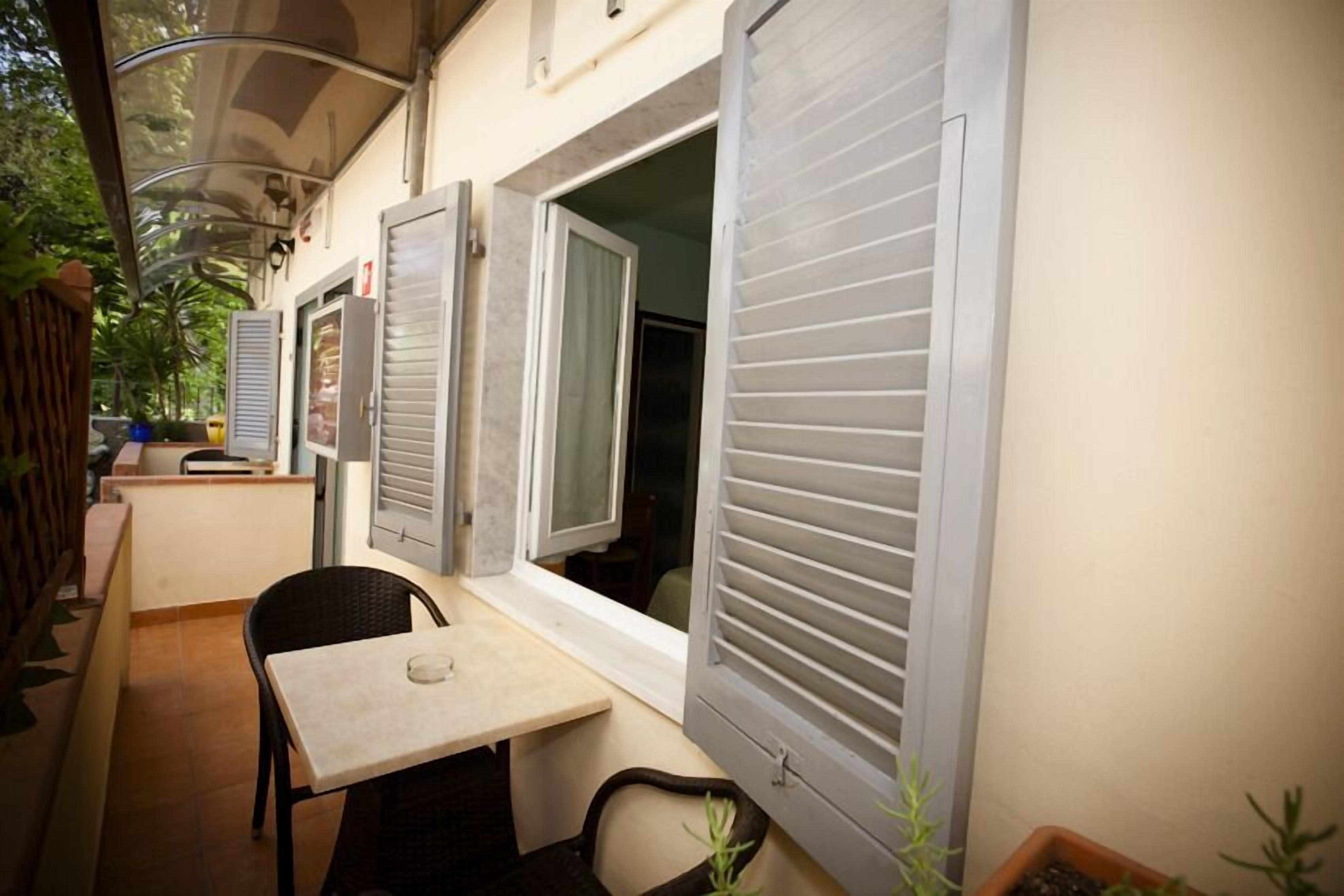 Ein kleiner Außenbereich mit Tisch und Stühlen, ein Fenster mit Rollläden und einem Blumentopf.