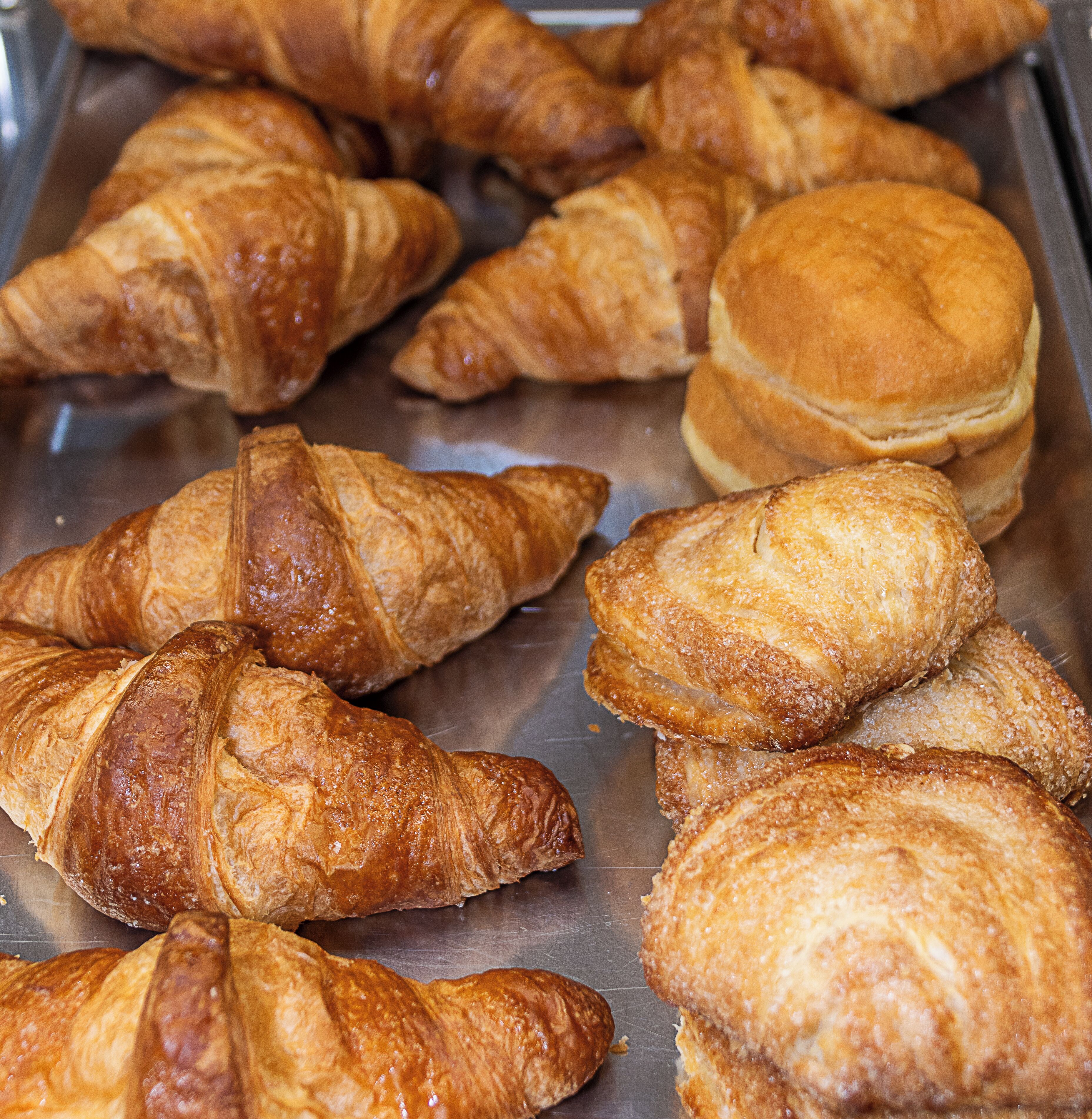 A variety of pastries, including croissants and bread rolls, displayed on a metal tray.