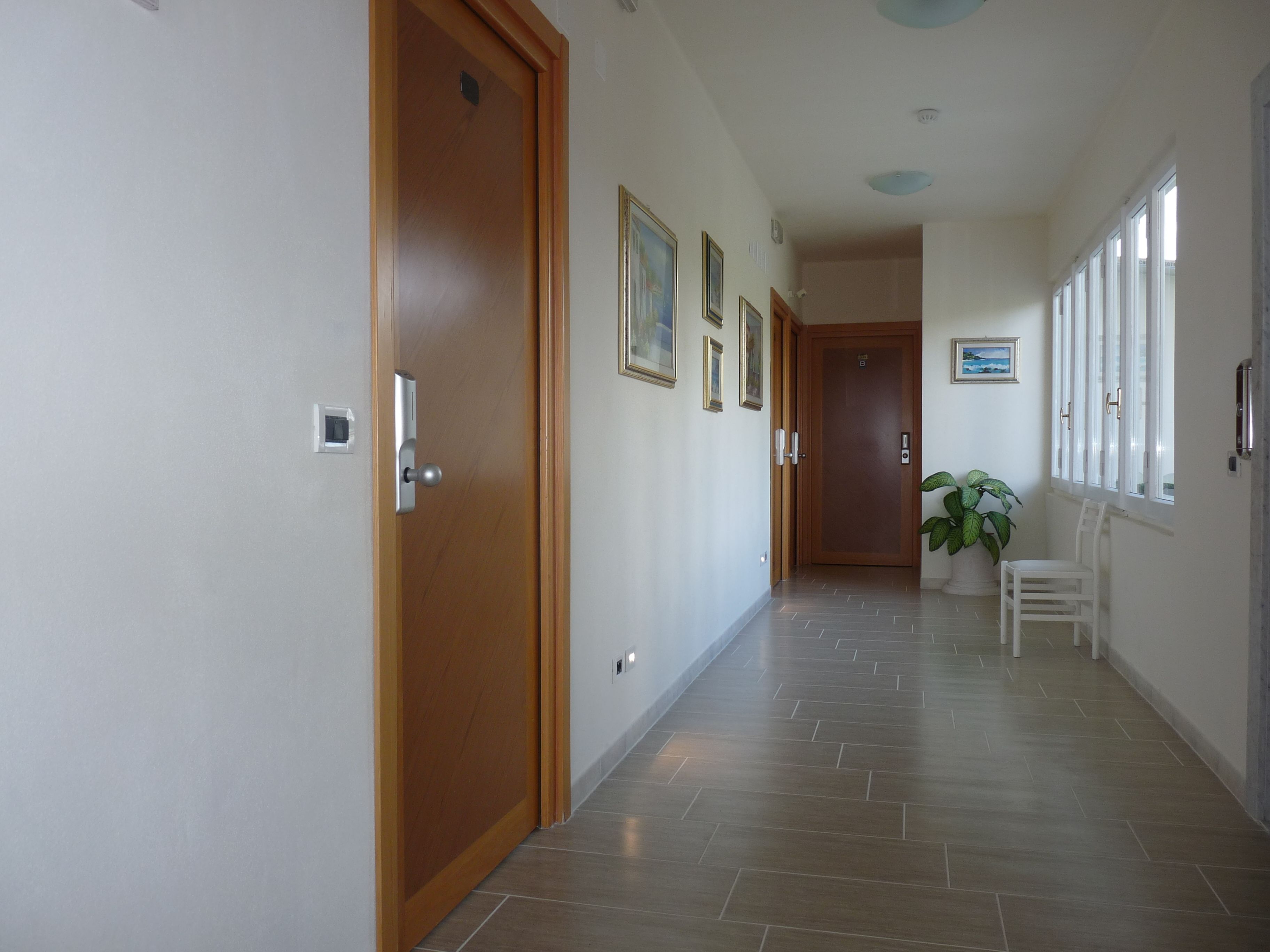 Um corredor com portas de madeira, soalho em azulejos e quadros nas paredes.
