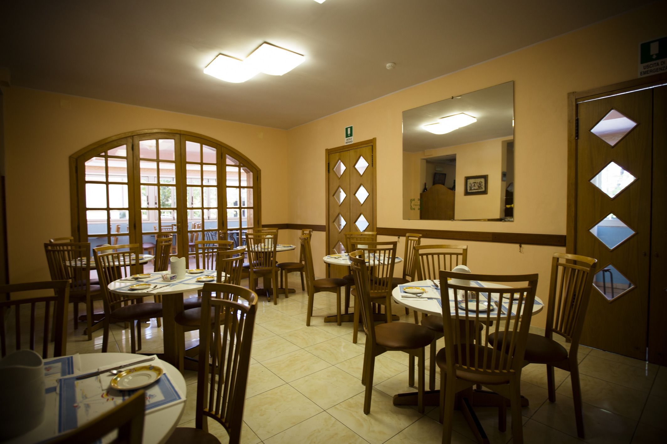 A dining area with multiple tables and chairs, a large arched window, and a mirror on the wall.