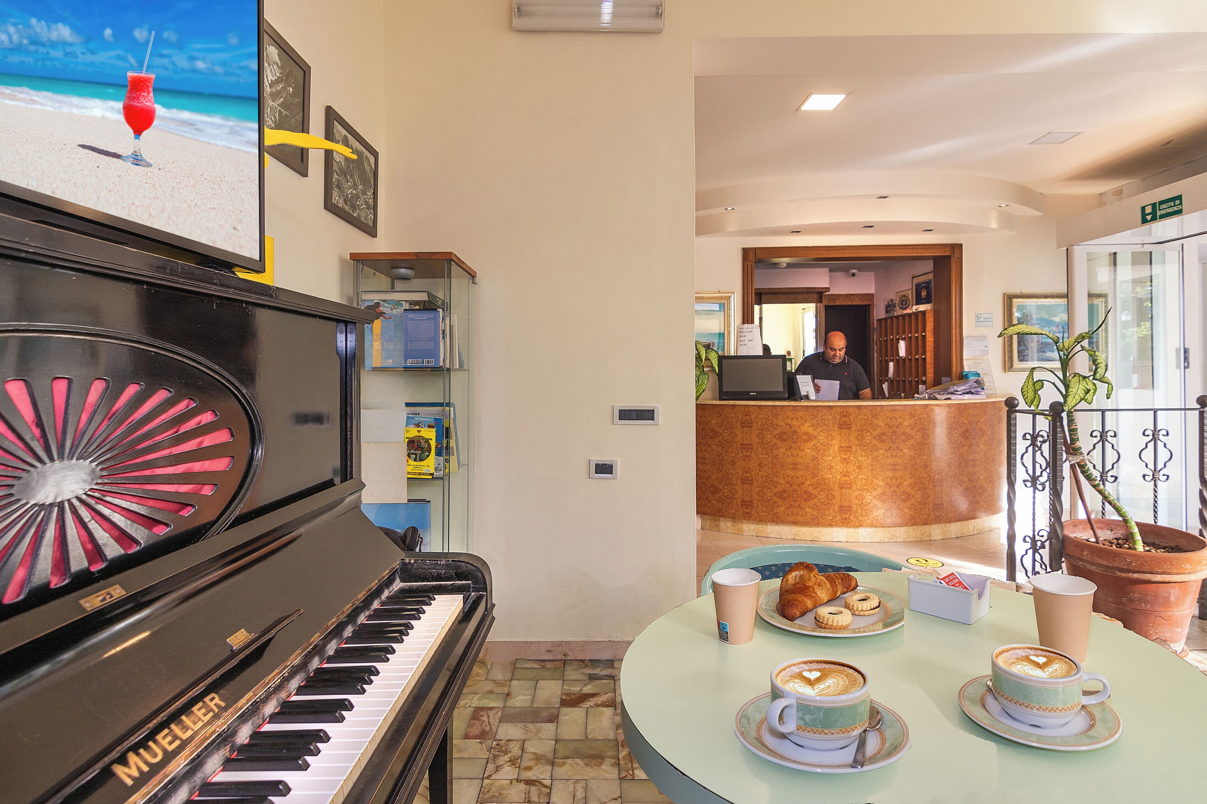 Un piano, una recepción y un comedor con cruasanes y tazas de café.