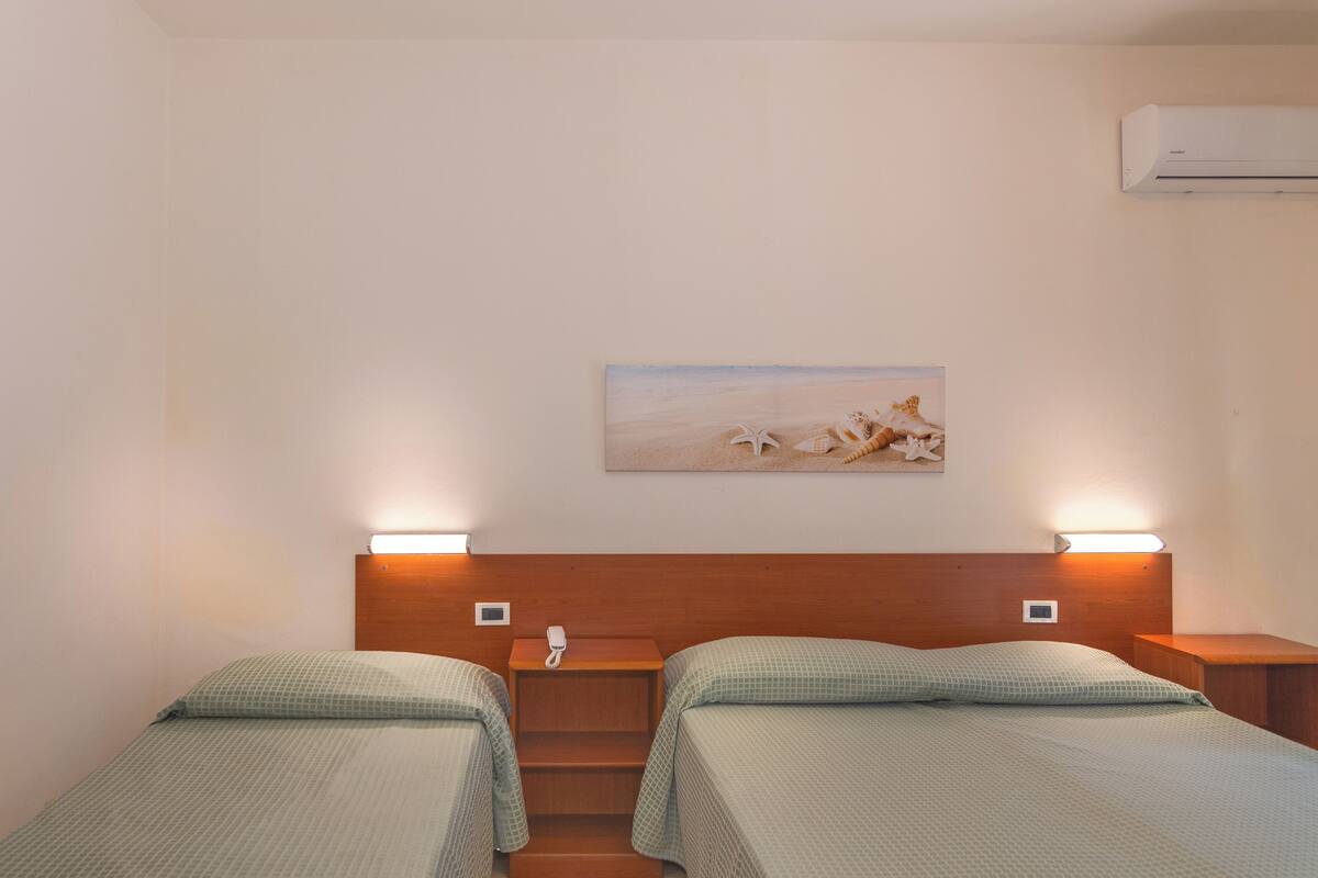 A hotel room with two beds, a painting of a beach scene, and a staircase.