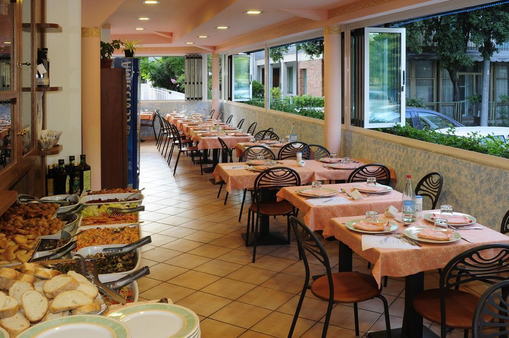A buffet-style restaurant with multiple tables and chairs, a variety of food items on display, and a view of the street outside.