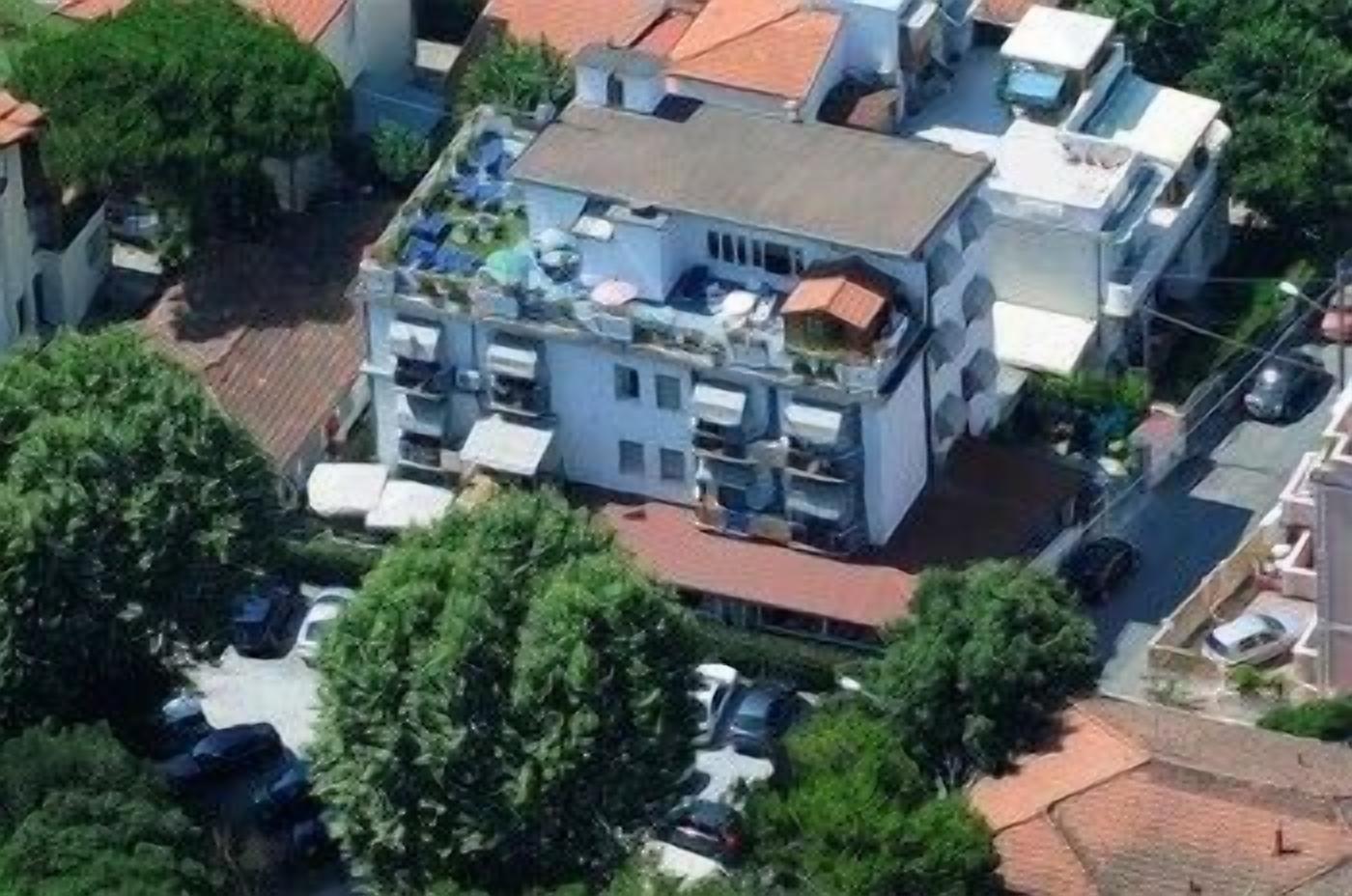 A multi-story residential building with balconies, a parking area, and surrounding greenery.