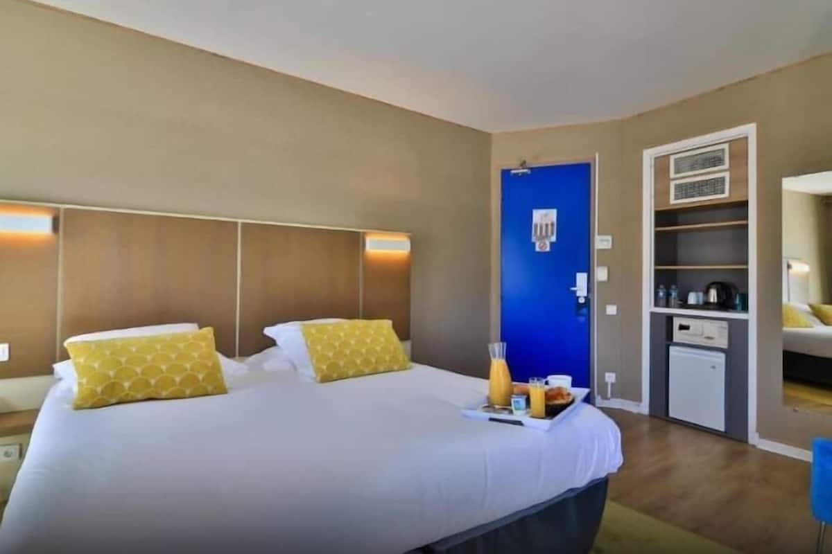 A hotel room with a large bed, bedside tables, a wardrobe, and a blue door.