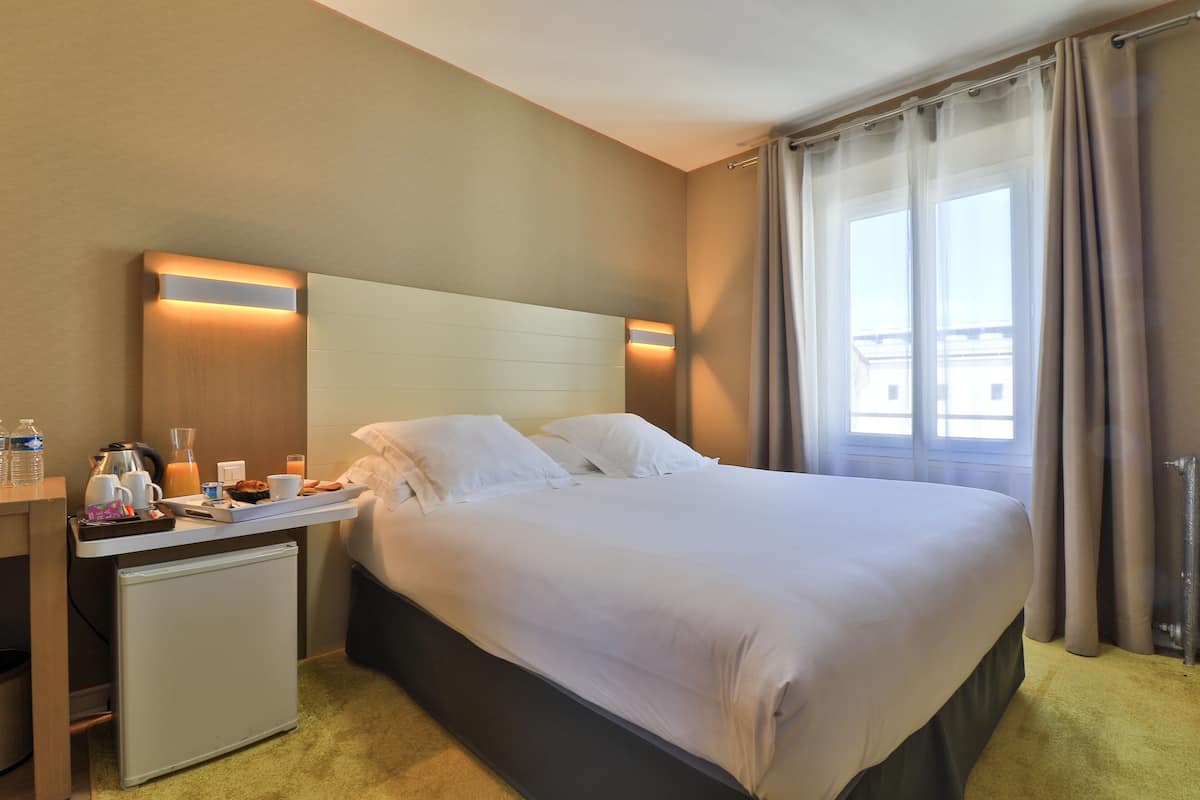 A hotel room with a bed, bedside table, and a window with curtains.