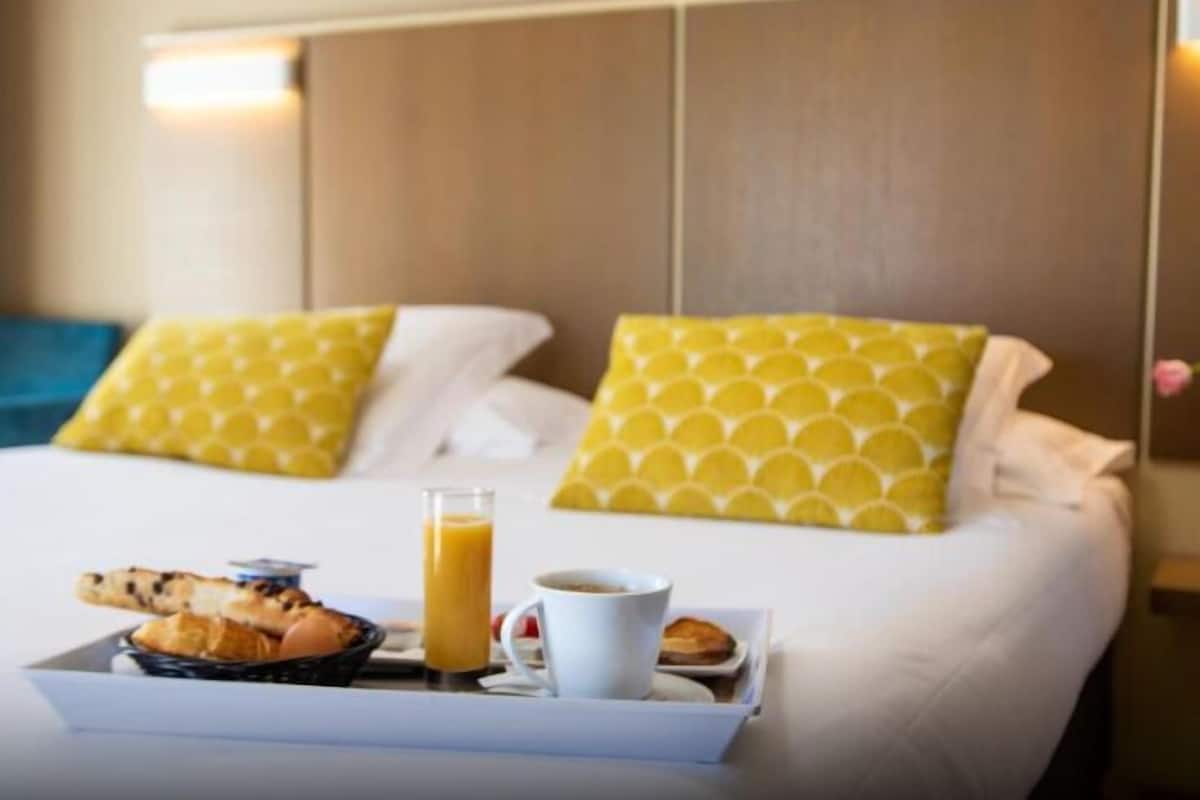A hotel room with a bed, pillows, a tray with food and a drink, and a nightstand.