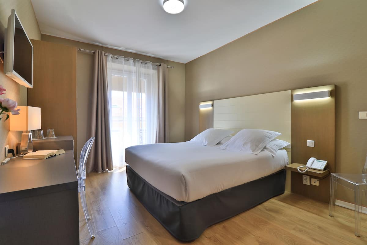 A modern hotel room with a large bed, bedside tables, a desk with a chair, a flat-screen TV, and a window with curtains.