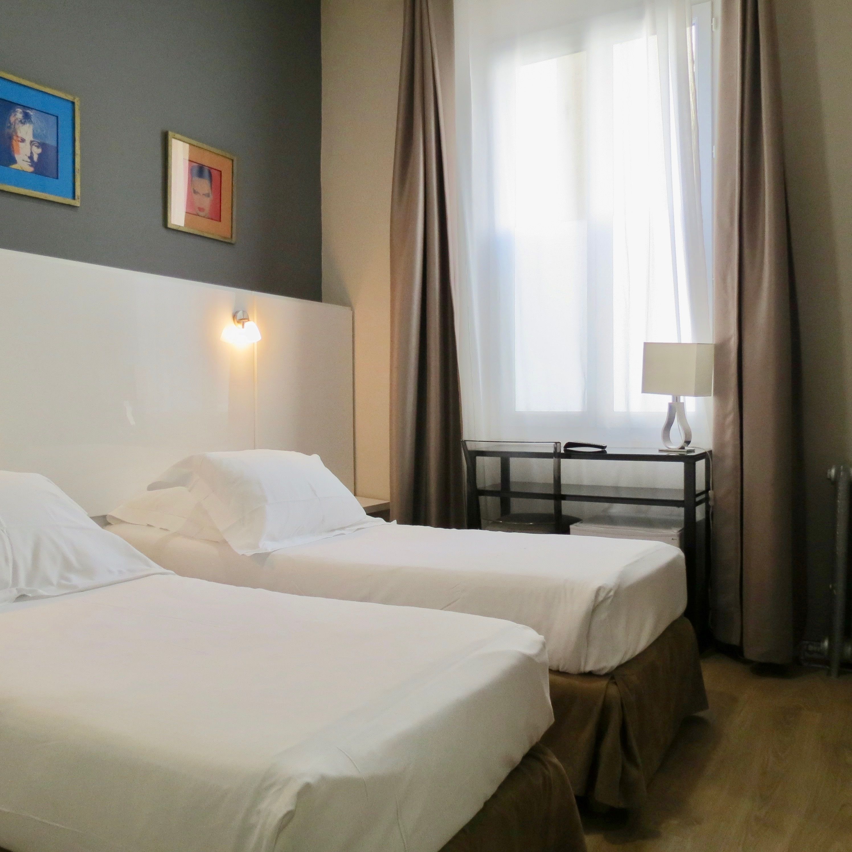 A hotel room with two beds, a desk, and a window with curtains.