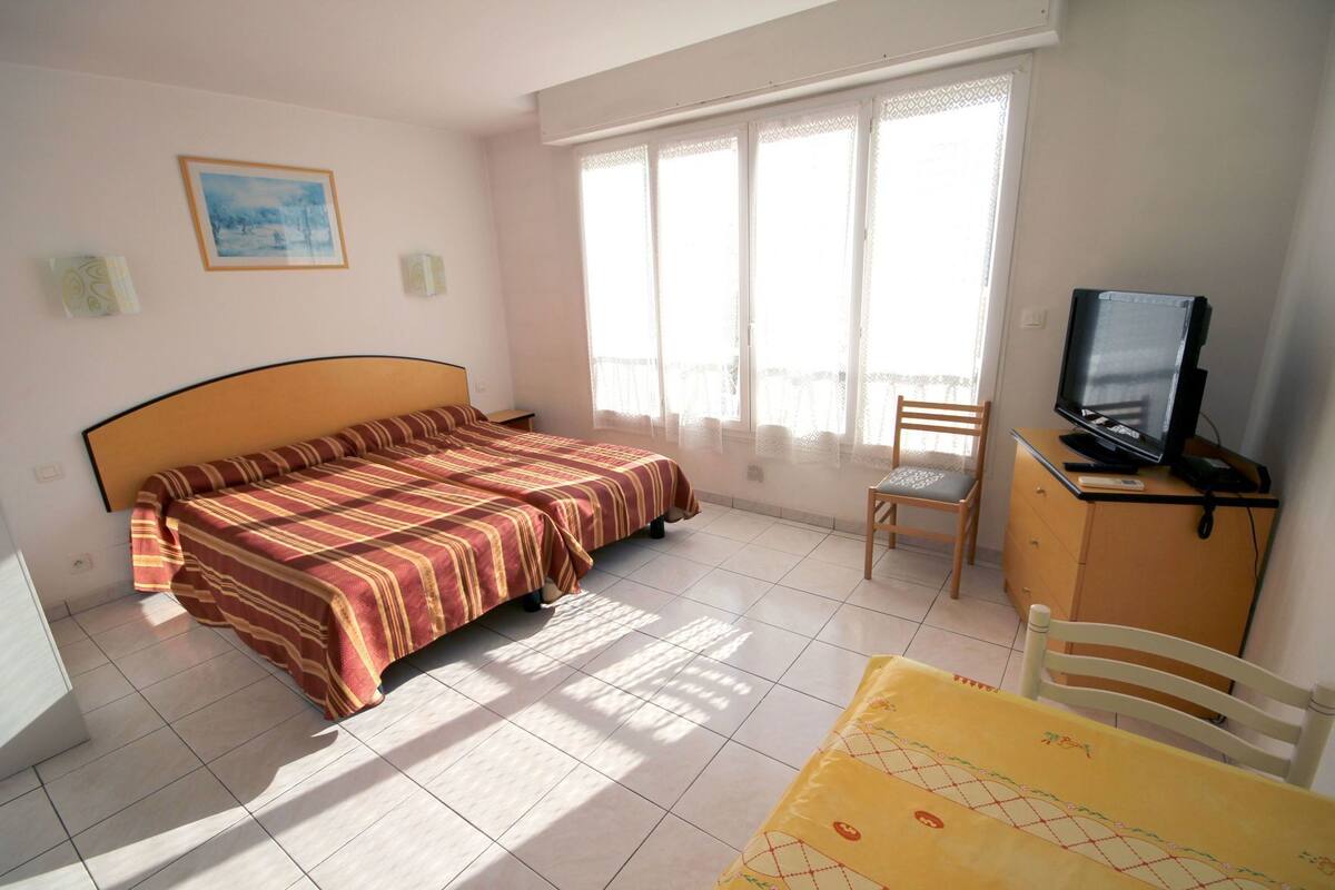 A bedroom with a bed, a TV, a chair, and a table.
