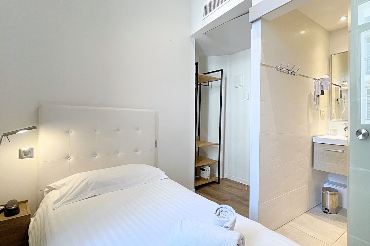 A hotel room with a bed, a nightstand, a bathroom with a sink, mirror, and a towel rack.