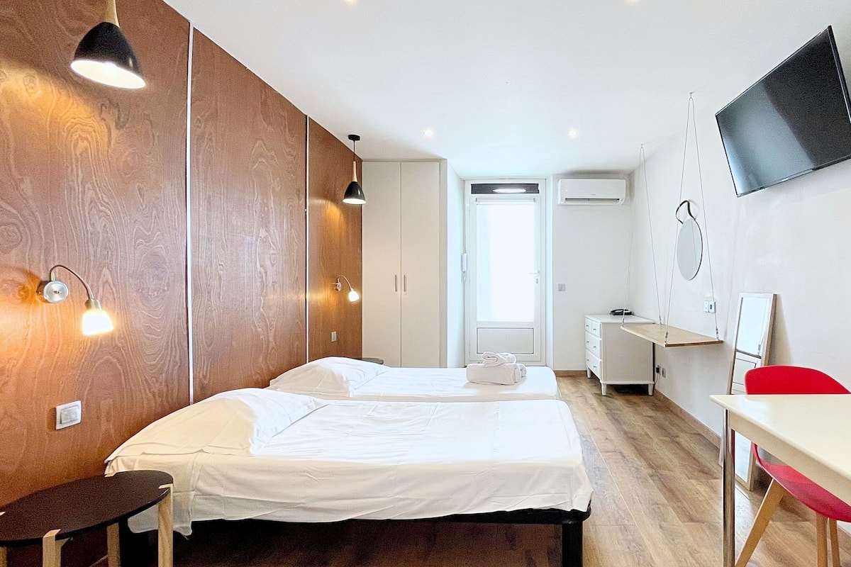 A hotel room with two beds, a desk, a chair, a TV, and a wardrobe.