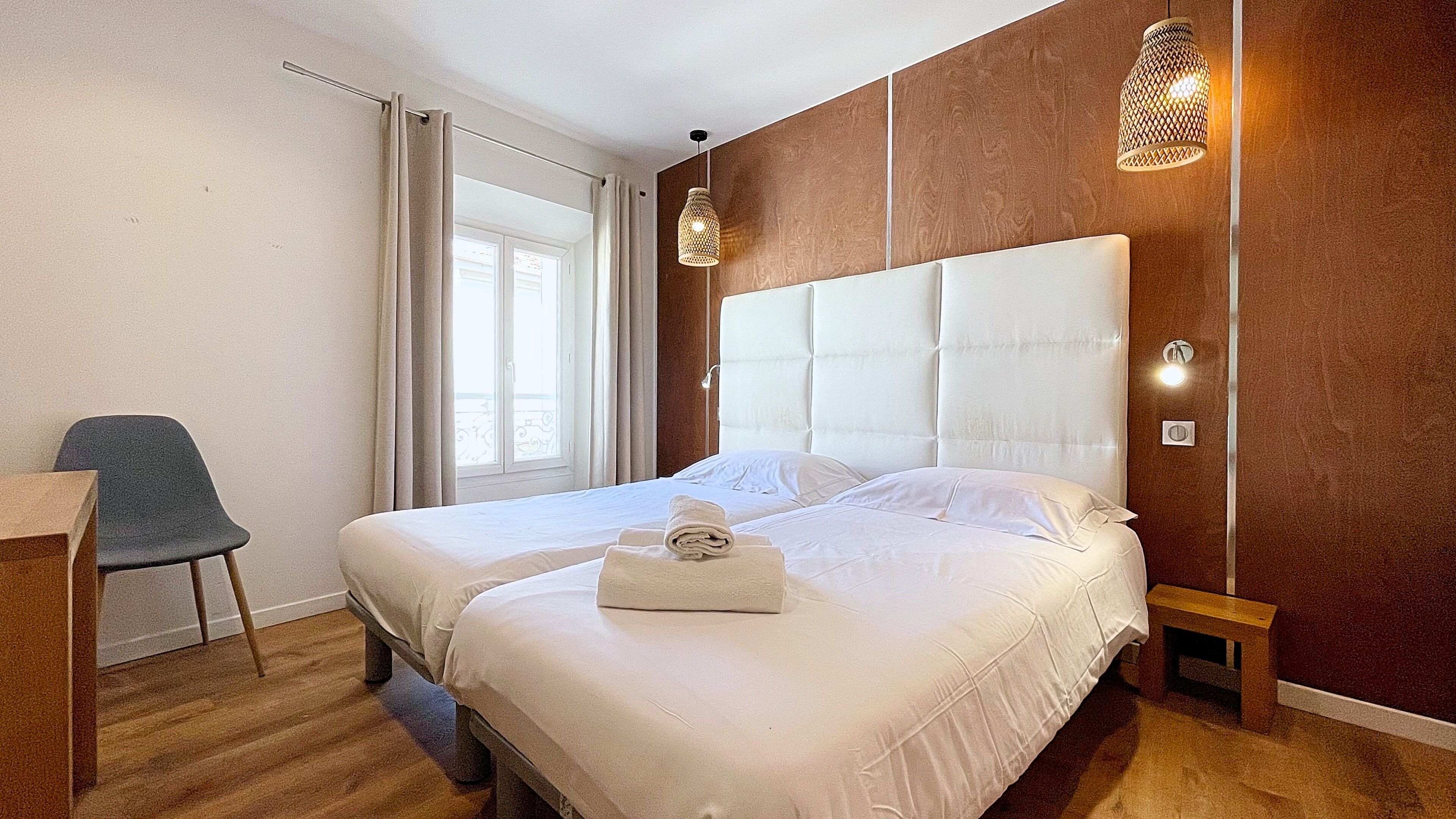 A hotel room with a large bed, a chair, a desk, and a window with curtains.