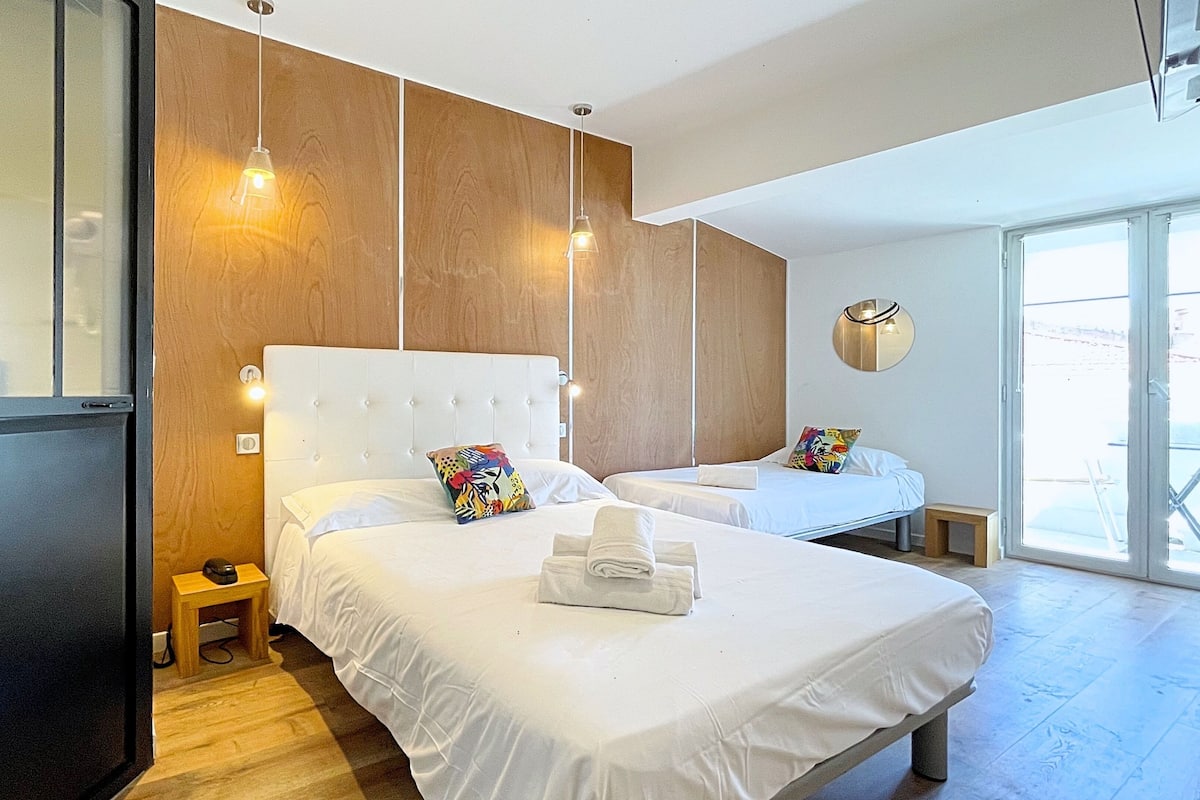 A hotel room with two beds, a wooden accent wall, a large window, and a small bedside table with a lamp.