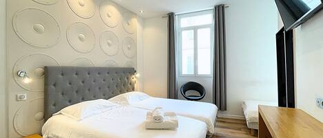 Habitación de hotel con una cama grande, un escritorio pequeño, una silla, televisión y ventana con cortinas.