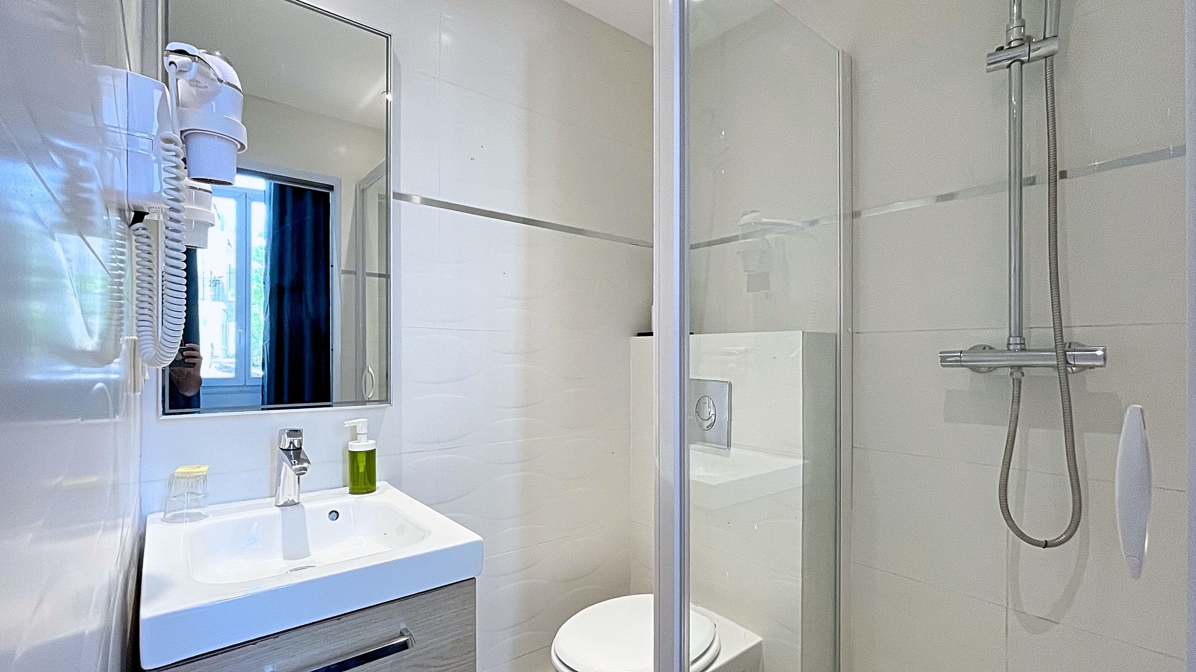 Un baño moderno con cabina de ducha de vidrio, un lavamanos blanco con espejo encima y un inodoro visible a través del vidrio.